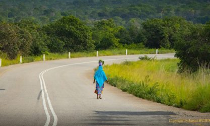 I woman with a basket on her head walks along a tarred road.