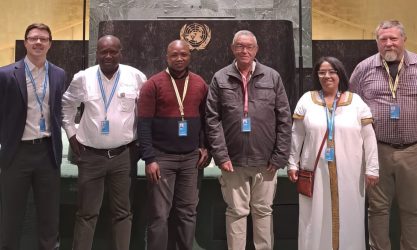 Six people posing in front of the UN emblem.