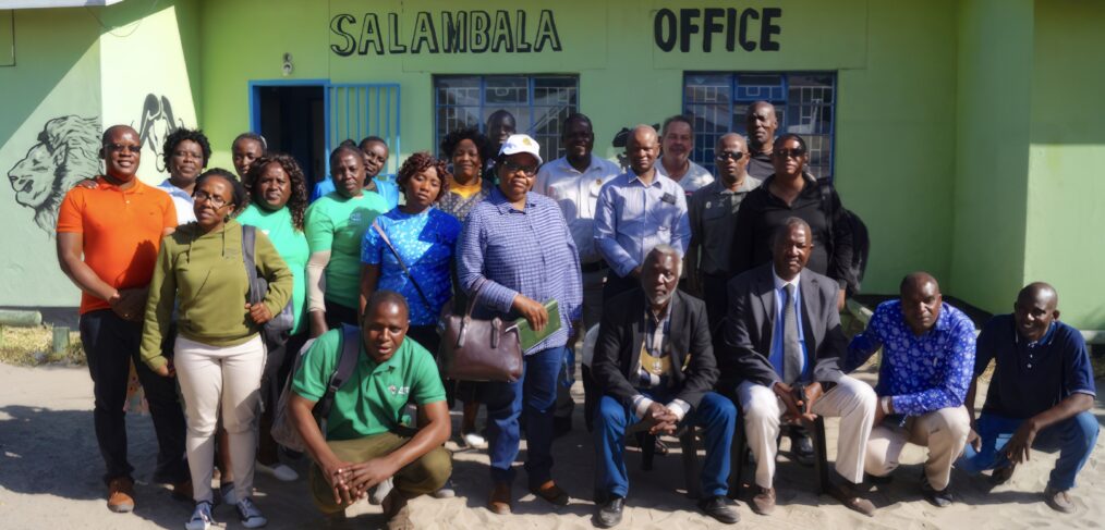 A group poses in front of a green painted office building.