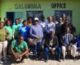 A group poses in front of a green painted office building.