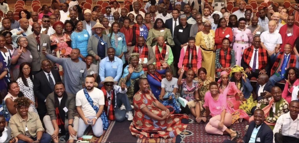 Around 50 people in a meeting room pose for a group photograph.