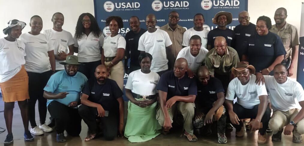 Twenty-two men and women pose for a photo in front of a USAID banner.