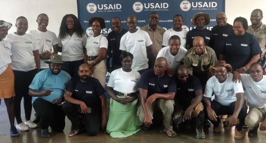 Twenty-two men and women pose for a photo in front of a USAID banner.