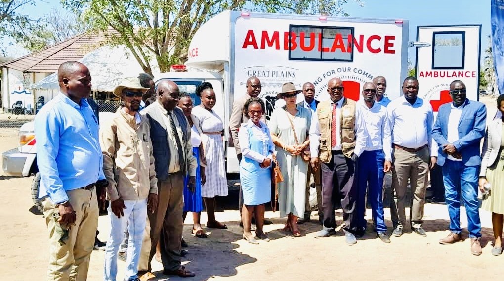 A group of people stand, smiling, in front of an ambulance.