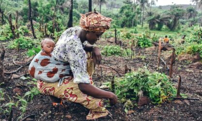A woman gardens with a child strapped to her back.