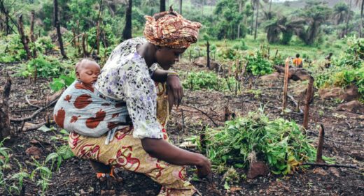 A woman gardens with a child strapped to her back.