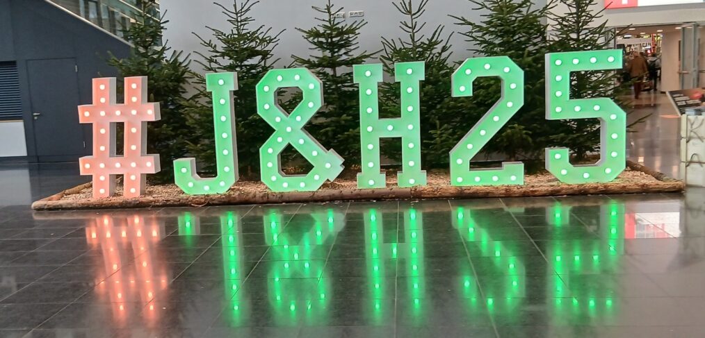A green sign picked out in lights of the hashtag #J&H25