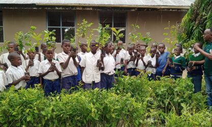 A group of schoolchildren holding baby trees ready to plant.